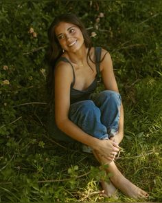 a woman sitting in the grass with her legs crossed and looking at the camera smiling