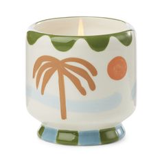 a ceramic candle holder with a palm tree on the front and an orange dot in the middle