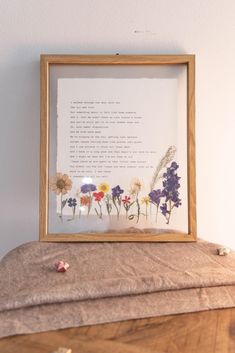 a wooden frame with some flowers in it on top of a table next to a pillow