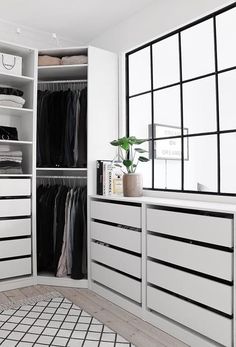 a white closet with drawers and clothes hanging on the wall next to a large window