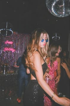 a woman in a sequin dress dancing at a party with disco balls behind her