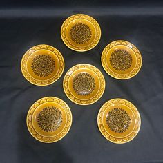 six yellow plates with designs on them sitting on a black tableclothed surface in the shape of a flower