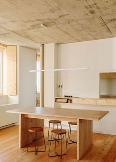 an empty kitchen with wooden floors and white walls, along with two stools at the table