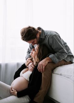 a pregnant couple cuddles on the bed while looking into each other's eyes