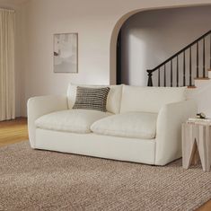 a white couch sitting on top of a wooden floor next to a stair case in a living room