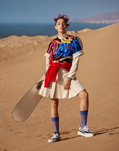 a woman standing in the sand with a skateboard on her feet and wearing a skirt