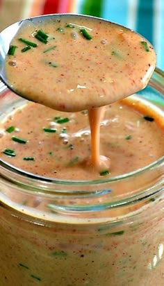 a spoon full of dressing being held up by a jar filled with sauce and garnished with parsley