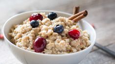 a white bowl filled with oatmeal topped with cherries and cinnamon sticks