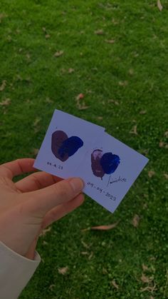 someone is holding up two pieces of paper with hearts drawn on them in the grass