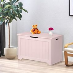 a teddy bear sitting on top of a pink box next to a chair and potted plant