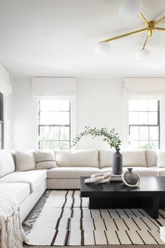 a living room with white couches and black coffee table in front of two windows