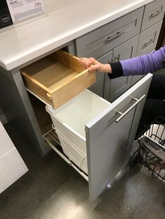 a woman is opening the drawers of a kitchen cabinet in order to find what's right for her