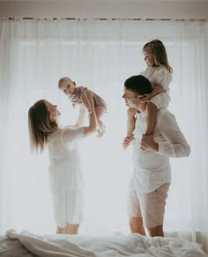 a woman holding a baby while standing next to two other women in front of a window