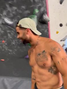 a shirtless man standing in front of a climbing wall