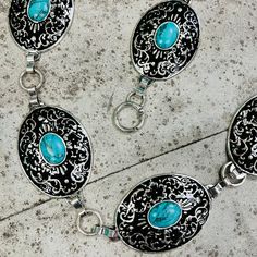 The At the Mountain Top Chain Link Belt is a silver and turquoise stone concho belt. The concho's have a black background with a floral scroll pattern design. The concho's are 2" X 2 1/2" in size. And the belt is 46" long with the adjustable chain links. Scroll Pattern Design, Concho Belt, Scroll Pattern, Chain Links, Mountain Top, Turquoise Stone, The Mountain, Black Background, Chain Link