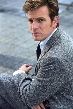 a man sitting on the ground wearing a suit and tie with his hand on his hip