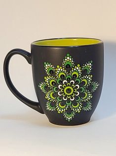 a black coffee cup with green and white designs on it's side, sitting against a white background