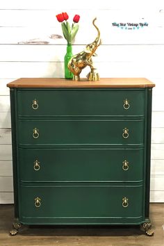 a green dresser with gold handles and flowers on top