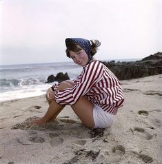 a woman sitting on top of a sandy beach next to the ocean with an american flag shirt