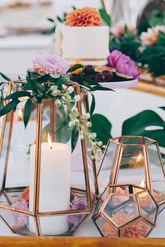 two candles are sitting on a table with flowers and greenery in front of them