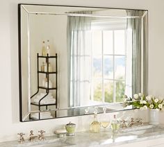 a bathroom mirror sitting on top of a white counter next to a sink and window