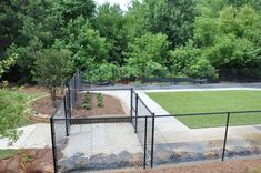 an outdoor tennis court surrounded by trees and grass in the middle of a fenced area