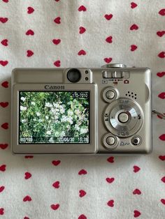 a digital camera sitting on top of a white and red table cloth with hearts drawn on it