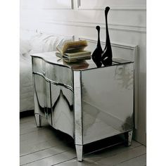 a mirrored side table with two black vases on top and books in front of it