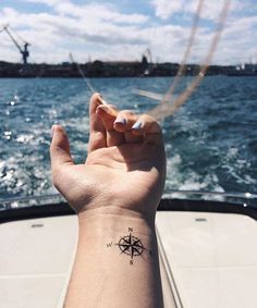 a person's hand with a compass tattoo on their left wrist and the ocean in the background