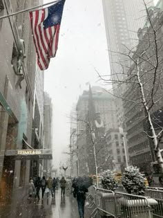 people walking in the snow on a city street with an american flag hanging above them