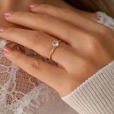 a woman's hand wearing a gold ring with a diamond on it and a white lace top