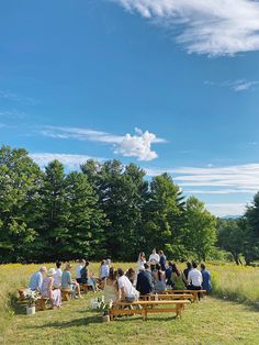 a group of people sitting on top of a lush green field under a blue sky