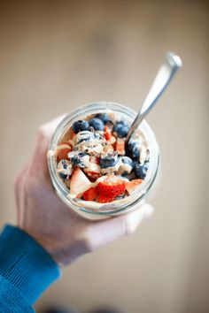 a person is holding a bowl of fruit and yogurt with a spoon in it