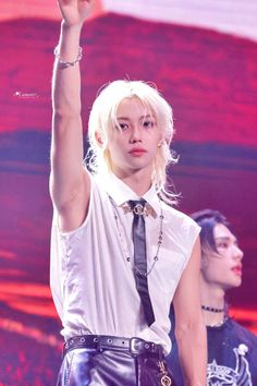 a woman with blonde hair wearing a white shirt and black tie holding her hand up in the air