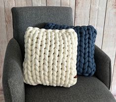 two blue and white knitted pillows sitting on a gray chair against a wooden wall