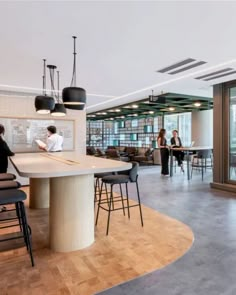 people are sitting at tables in the middle of an open concept office with large windows