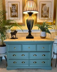 a lamp on top of a dresser in a room with pictures and potted plants