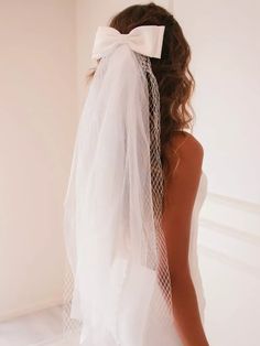 a woman wearing a veil with a white bow on it's head is standing in front of a wall