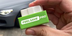 a hand holding a green and white battery in front of a car with the word eco max fuel saver on it