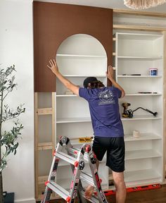 a man standing on a ladder in front of a book shelf and painting the walls