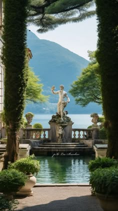 an outdoor fountain surrounded by greenery and trees with a mountain in the back ground