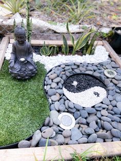 a buddha statue sitting on top of a lush green field next to a rock garden