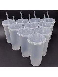 plastic cups with straws are lined up on a black surface, ready to be used as drinks