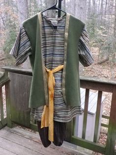 a green coat hanging on a wooden deck in the woods with trees and leaves behind it