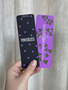 Introducing the Powerless Bookmark, the perfect accessory for avid readers! This bookmark comes in a sleek purple and black design that is sure to catch your eye. The bookmark is double-sided, providing twice the convenience and functionality of a regular bookmark. Crafted from high-quality materials, this matte-finished bookmark is designed to last for years. It's perfect for keeping your place in your favorite book or textbook without damaging the pages. Plus, its lightweight design makes it e Bookmarks Handmade Simple, Powerless Bookmark, Black Bookmark, Purple Bookmark, Powerless Trilogy, Books Bookmark, Cool Bookmarks, Reading Accessories, Fantasy Books To Read