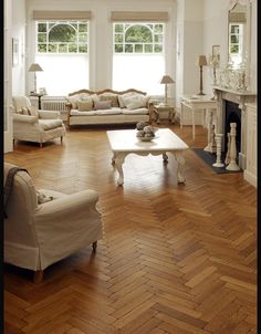 a living room filled with white furniture and wooden floors next to a fire place oven