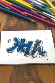 Simple blue graffiti art drawing on paper with colorful pencils arranged nearby. Easy Graffiti Drawing Ideas, Drawings Ideas For Beginners, Graffiti Drawing Ideas, Graffiti Drawings, Cartoon Characters Sketch, Easy Graffiti, Easy Graffiti Drawings, Diy Graffiti, Drawings Ideas