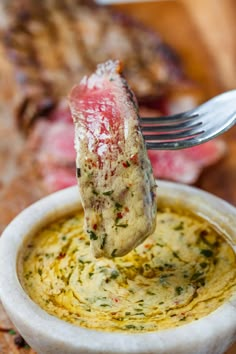 a piece of meat is being lifted from a small bowl with some sauce on it