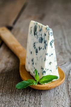 a piece of blue cheese on a wooden plate with mint sprig next to it