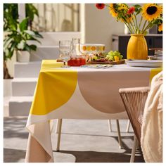 a yellow vase filled with flowers sitting on top of a table next to a white and yellow table cloth